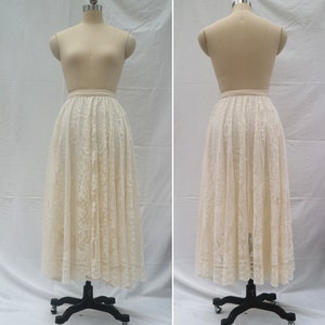 May include: A white lace skirt with a full, flowing silhouette. The skirt is made of delicate lace with a floral pattern. It is shown on a dress form.