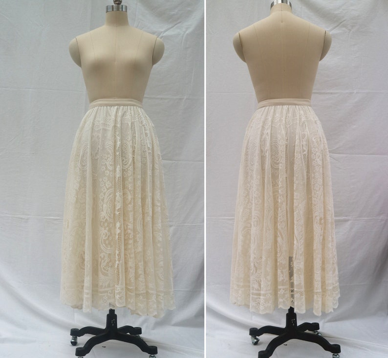 May include: A white lace skirt with a full, flowing silhouette. The skirt is made of delicate lace with a floral pattern. It is shown on a dress form.