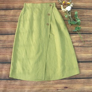 May include: A light green linen skirt with a wrap-around design and a button closure. The skirt has a simple, casual style.