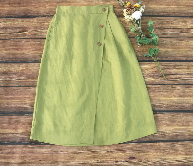May include: A light green linen skirt with a wrap-around design and a button closure. The skirt has a simple, casual style.