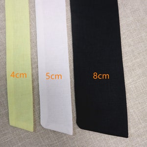May include: Three fabric strips in different colors and widths. The strip on the left is light yellow and measures 4 cm. The middle strip is white and measures 5 cm. The strip on the right is black and measures 8 cm.