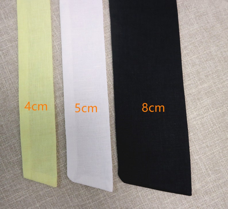 May include: Three fabric strips in different colors and widths. The strip on the left is light yellow and measures 4 cm. The middle strip is white and measures 5 cm. The strip on the right is black and measures 8 cm.