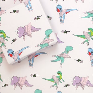 May include: White wrapping paper with a repeating pattern of pink, green, and purple dinosaurs wearing pink tutus. The dinosaurs are in various poses, including dancing and standing. There are also small pink roses scattered throughout the pattern.