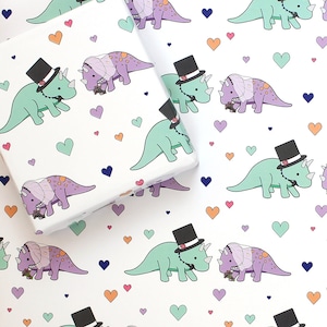 May include: White wrapping paper with a repeating pattern of green and purple dinosaurs wearing top hats and veils. The dinosaurs are holding bouquets of flowers. The background is filled with small hearts in various colors.