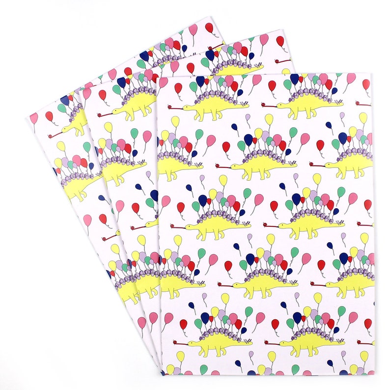 May include: A pack of four wrapping paper sheets featuring a repeating pattern of yellow dinosaurs with purple, pink, red, blue, and green balloons. The dinosaurs are blowing party horns.