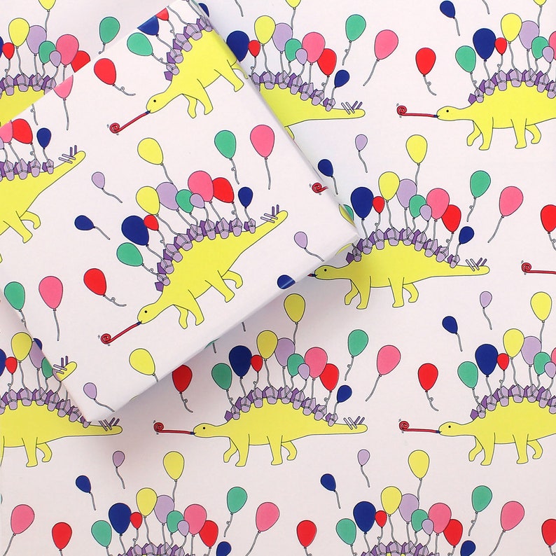 May include: White wrapping paper with a repeating pattern of yellow dinosaurs with colourful balloons on their backs. The dinosaurs are blowing party horns.