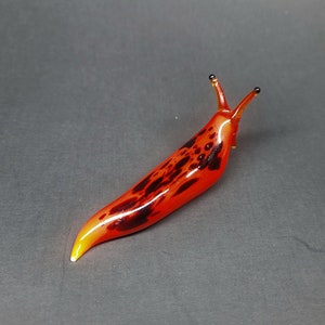 Könnte beinhalten: Eine Glasskulptur eines roten und schwarzen Schneckens mit einer gelben Spitze. Die Schnecke ist aus Glas und hat ein realistisches Aussehen.