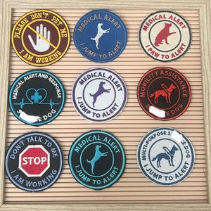 May include: A collection of embroidered patches with various designs and text. The patches include phrases like "Medical Alert," "I Jump to Alert," and "Don't Pet Me." The patches feature dog silhouettes and other graphics, with a variety of colors.