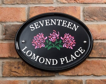 May include: Black oval house number sign with white text that reads "SEVENTEEN LOMOND PLACE". The sign has three pink flowers with green leaves.