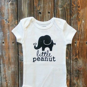May include: White baby onesie with a black silhouette of an elephant and the text "little peanut".