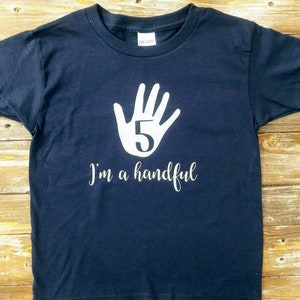 May include: A dark blue t-shirt with a white handprint and the number 5 inside. The text "I'm a handful" is printed below the handprint.