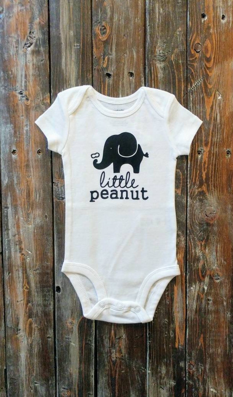 May include: White baby onesie with a black silhouette of an elephant and the text "little peanut".