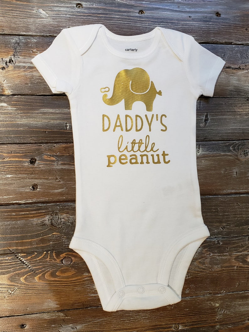 May include: White baby onesie with a gold elephant and the text "Daddy's little peanut".