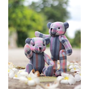 May include: Two plaid fabric teddy bears, one pink and blue, the other blue and pink, standing on a path with white flower petals scattered around them.