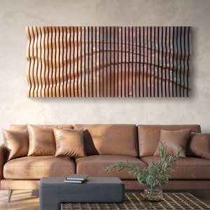Könnte beinhalten: Ein großes Wandkunstwerk aus Holz mit einem wellenförmigen, vertikalen Lamellendesign. Das Kunstwerk ist über einem braunen Ledersofa mit mehreren Wurfkissen angebracht. Der Raum hat eine moderne, minimalistische Ästhetik mit einer Backsteinmauer und einer Stehleuchte.