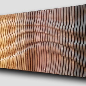 Può includere: Opera d'arte da parete in legno con un design a onde. Il pezzo è costruito con doghe di legno verticali, creando un effetto tridimensionale e strutturato. La sfumatura di colore passa dal marrone chiaro allo scuro, aggiungendo profondità e interesse visivo.