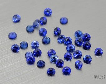 May include: A collection of loose round blue sapphires, scattered on a silver surface.