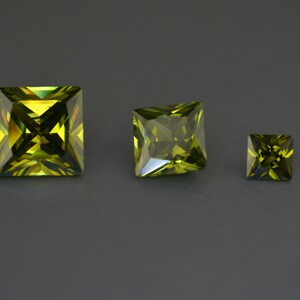 May include: Three green square-shaped gemstones of different sizes. The largest gemstone is in the center, the medium-sized gemstone is to the left, and the smallest gemstone is to the right.