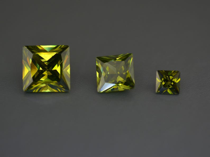 May include: Three green square-shaped gemstones of different sizes. The largest gemstone is in the center, the medium-sized gemstone is to the left, and the smallest gemstone is to the right.