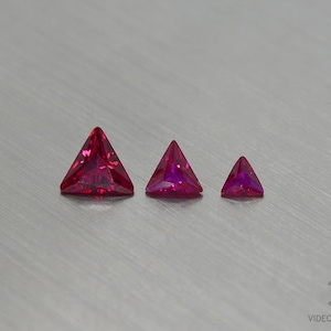 May include: Three triangular red gemstones of varying sizes. The largest gemstone is on the left, the smallest is on the right.