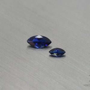 Könnte beinhalten: Zwei blaue Saphire in Marquise-Form, einer größer als der andere, auf silbernem Hintergrund.