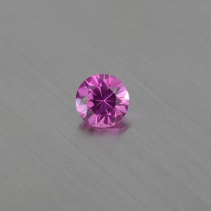 Pode incluir: Uma gema rosa redonda e facetada com um padrão em forma de estrela no centro.