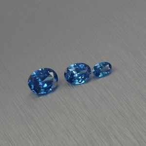 K&ouml;nnte beinhalten: Drei ovale blaue Edelsteine ​​in verschiedenen Gr&ouml;&szlig;en auf einer geb&uuml;rsteten silbernen Oberfl&auml;che.