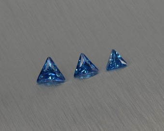 May include: Three triangular blue gemstones of varying sizes on a brushed silver surface.