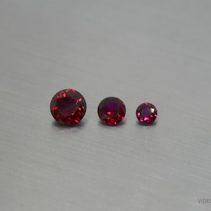 Puede incluir: Tres piedras preciosas rojas de diferentes tamaños. La piedra preciosa más grande es de color rojo oscuro, la piedra preciosa del medio es de color rojo claro y la piedra preciosa más pequeña es de color morado oscuro.