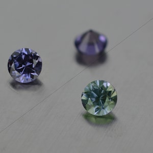 Può includere: Tre pietre preziose rotonde, una viola, una blu e una verde, su una superficie grigia.