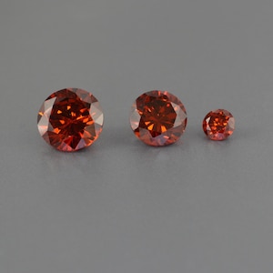Può includere: Tre pietre preziose rotonde e sfaccettate di diverse dimensioni. Le pietre preziose sono di colore rosso-arancio scuro.