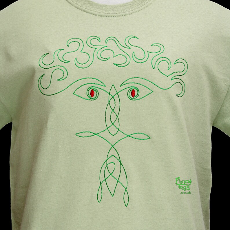 Pu&ograve; includere: Una maglietta verde chiaro con un disegno di nodo celtico ricamato in verde che rappresenta un viso con occhi rossi. Il disegno &egrave; centrato sulla maglietta. Il testo "Fancy Lugs .co.uk" &egrave; ricamato nell'angolo in basso a destra della maglietta.