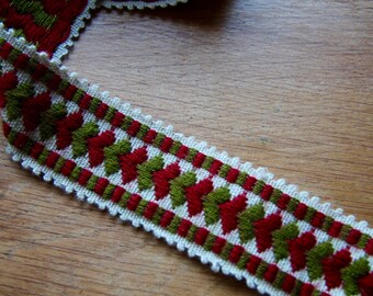 May include: A white, red, and green woven trim with a scalloped edge. The trim features a repeating pattern of red and green stylized leaves.