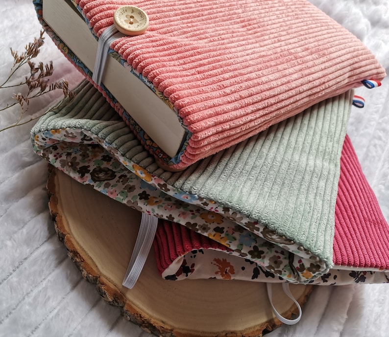 Pode incluir: Uma pilha de tr&ecirc;s capas de livros feitas de tecido de veludo cotel&ecirc;. A capa superior &eacute; rosa, a capa do meio &eacute; verde e a capa inferior &eacute; vermelha. As capas s&atilde;o decoradas com um padr&atilde;o floral.