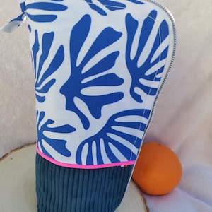 Peut inclure: Trousse à crayons en tissu avec un motif de feuilles bleues sur fond blanc. Le bas est en velours côtelé bleu foncé avec une bordure rose. Elle est dotée d'une fermeture éclair argentée et d'une petite boucle en tissu.
