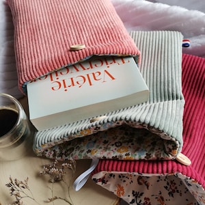 Pode incluir: Tr&ecirc;s capas de livro feitas de tecido de veludo cotel&ecirc; rosa, cinza e vermelho com forro estampado floral. As capas de livro est&atilde;o dobradas para revelar o livro interior, que tem o t&iacute;tulo "Val&eacute;rie Trierweiler" na lombada.