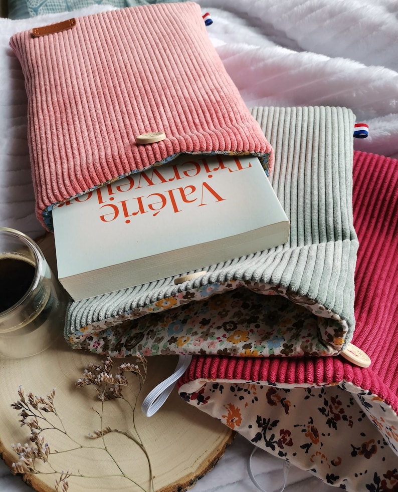 Pode incluir: Tr&ecirc;s capas de livro feitas de tecido de veludo cotel&ecirc; rosa, cinza e vermelho com forro estampado floral. As capas de livro est&atilde;o dobradas para revelar o livro interior, que tem o t&iacute;tulo "Val&eacute;rie Trierweiler" na lombada.