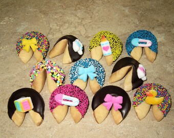 May include: A dozen fortune cookies decorated with colorful sprinkles and baby-themed toppers, including a bow, a bottle, a pacifier, and a duck. The cookies are half-dipped in chocolate.