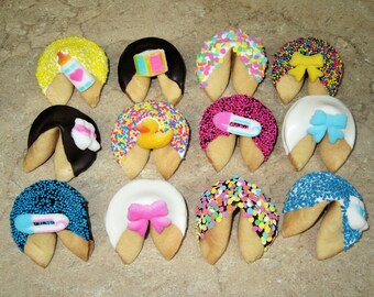 May include: Twelve fortune cookies decorated with colorful sprinkles and baby-themed decorations, including a baby bottle, a rubber duck, a bow, and a pacifier.