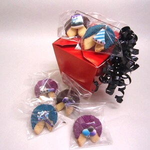 May include: A red takeout box with black ribbon and several fortune cookies. The fortune cookies are decorated with blue, purple, and brown sprinkles and small party hats. The cookies are individually wrapped in clear plastic.