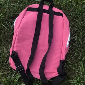May include: A pink canvas backpack with black adjustable straps. The backpack has a zipper closure and a white zipper pull.