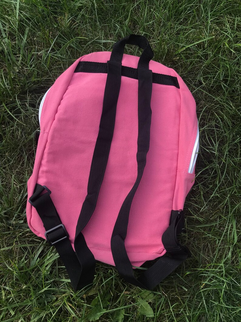 May include: A pink canvas backpack with black adjustable straps. The backpack has a zipper closure and a white zipper pull.