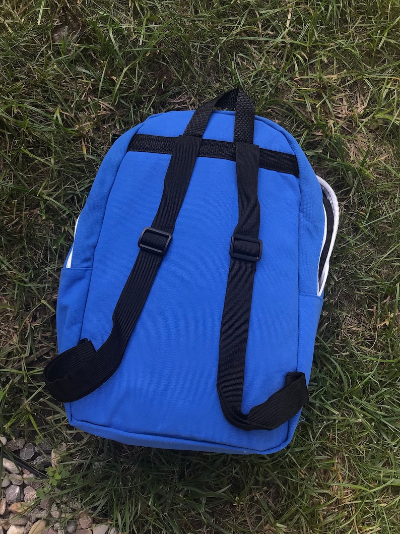 Pu&ograve; includere: Uno zaino blu con spalline nere e rifiniture bianche. Lo zaino ha una chiusura con cerniera e una piccola tasca sul davanti.