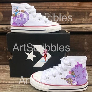 May include: A pair of white high-top canvas shoes with hand-painted Winnie the Pooh characters. One shoe features Piglet riding on a purple elephant, while the other shoe features Tigger. The shoes are in a box with the words "ArtScribbles" printed on it.
