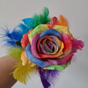 May include: A vibrant rainbow-colored rose with a multitude of petals, accented by colorful feathers in shades of blue, green, yellow, orange, and purple. The flower is a striking display of color and texture.