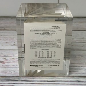 May include: A close-up of a clear acrylic paperweight with a document inside. The document is a bond prospectus for the American Educational Complex College District, Series 1994. The document includes the bond amount, maturity schedule, and the names of the underwriters, Mercantile Capital Markets and A.G. Edwards & Sons, Inc.