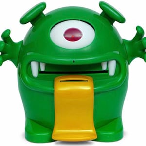 May include: A green monster-shaped piggy bank with a single eye, two small antennae, and a yellow coin slot. The bank has white teeth and outstretched arms, giving it a playful appearance. The coin slot is a bright yellow color.