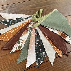 May include: A green, brown, and white fabric banner with a scalloped edge. The banner is made of different patterned fabrics, including floral, polka dot, and solid colors.