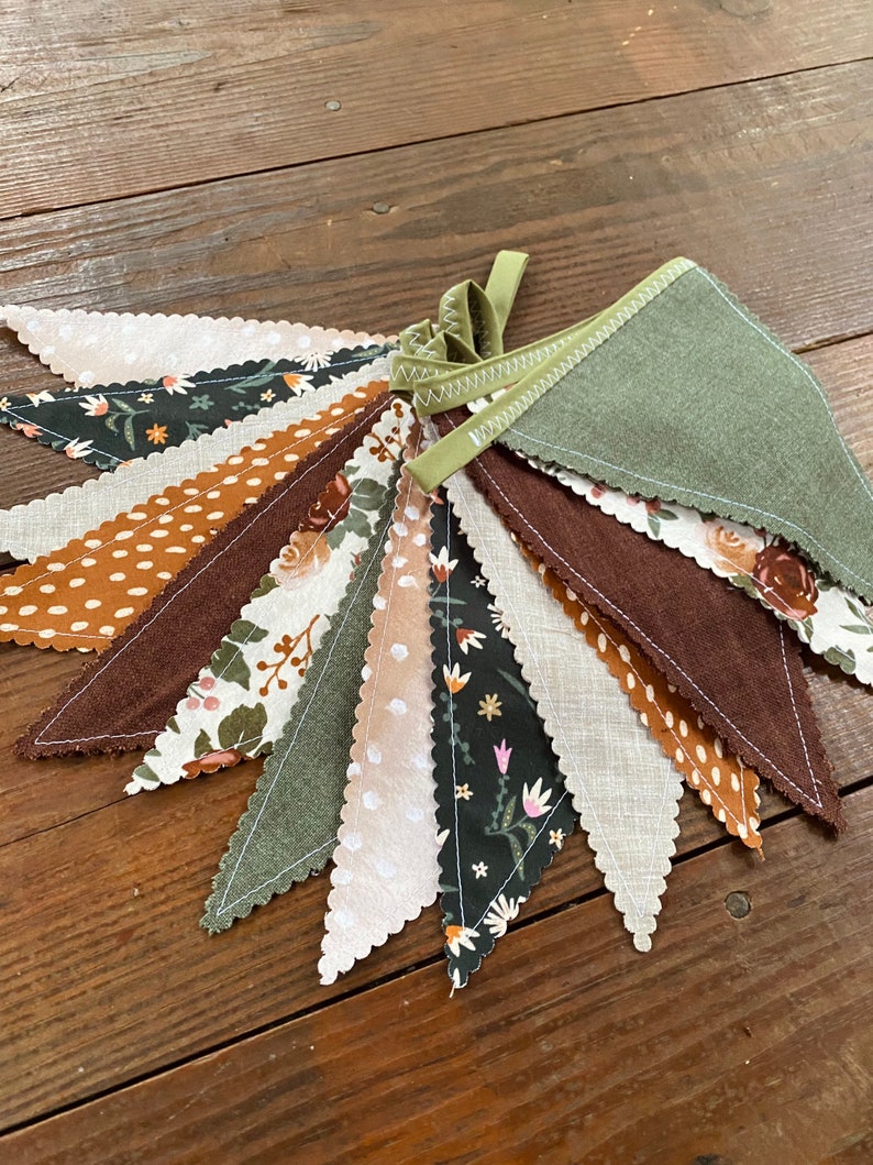 May include: A green, brown, and white fabric banner with a scalloped edge. The banner is made of different patterned fabrics, including floral, polka dot, and solid colors.