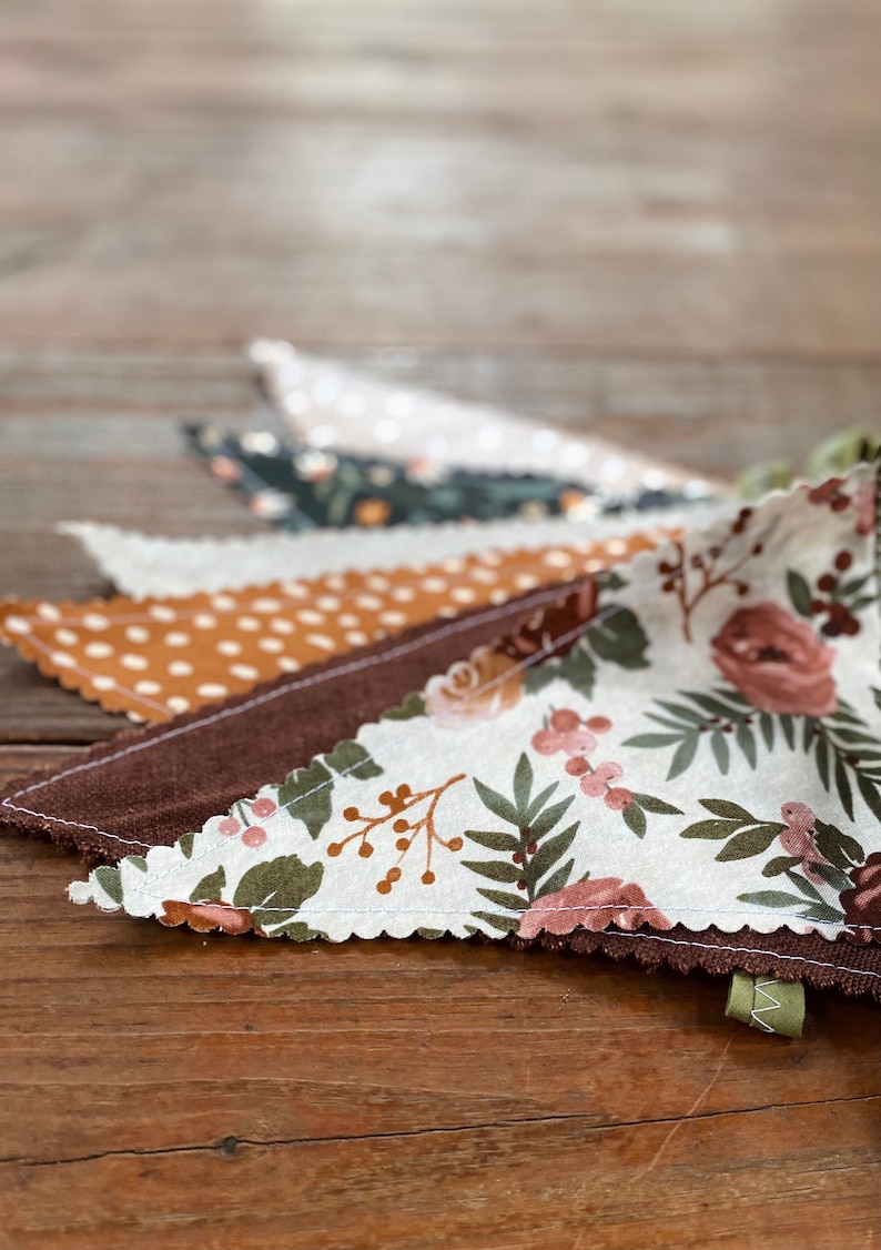 May include: A garland of fabric pennants with different patterns. The pennants are brown, white, and tan with floral and polka dot designs.
